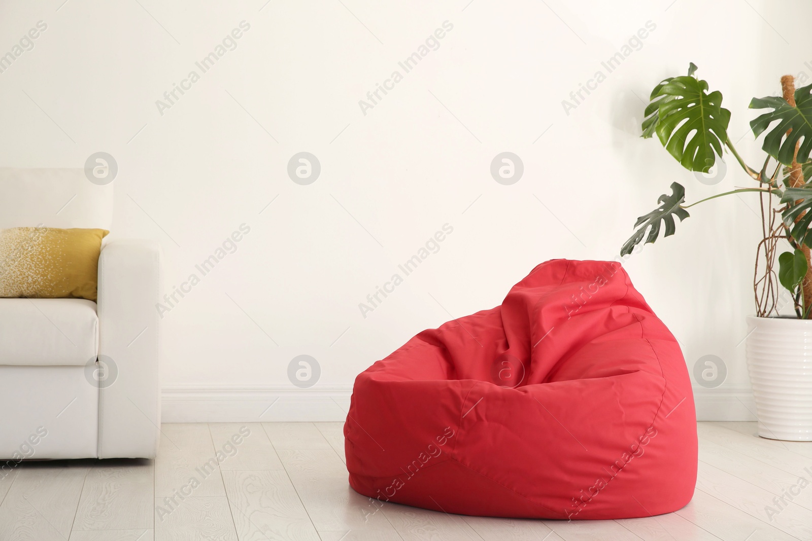 Photo of Red bean bag chair near light wall in room. Space for text