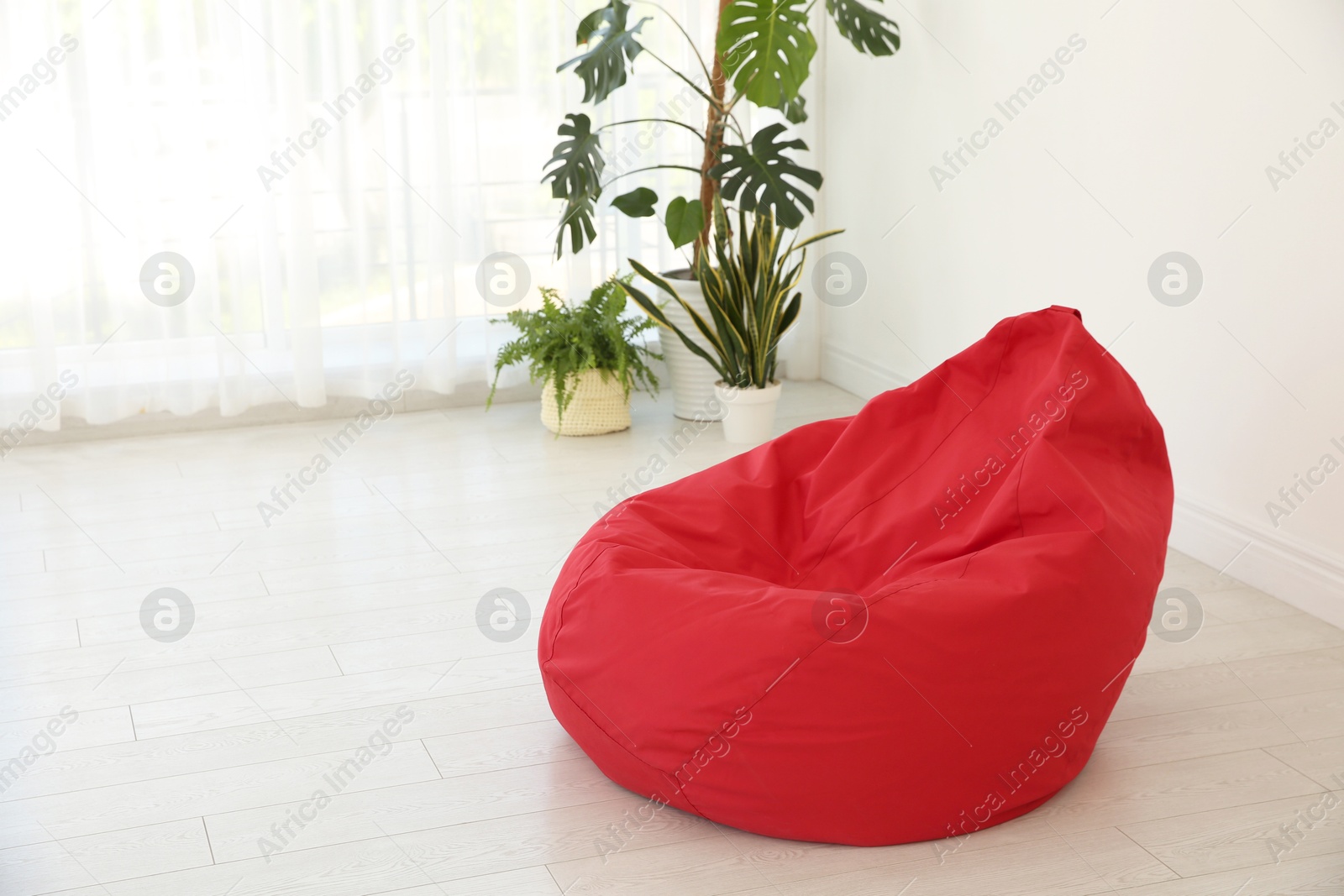 Photo of Red bean bag chair near light wall in room. Space for text