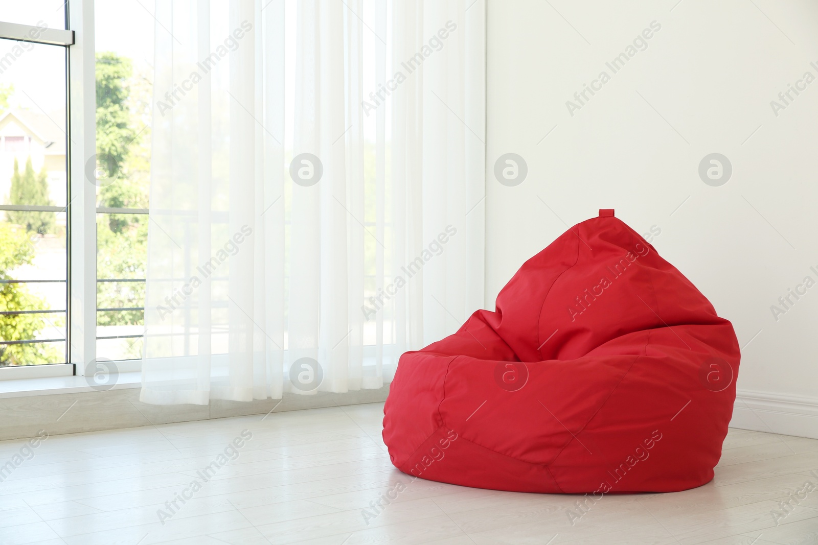 Photo of Red bean bag chair near window in room. Space for text