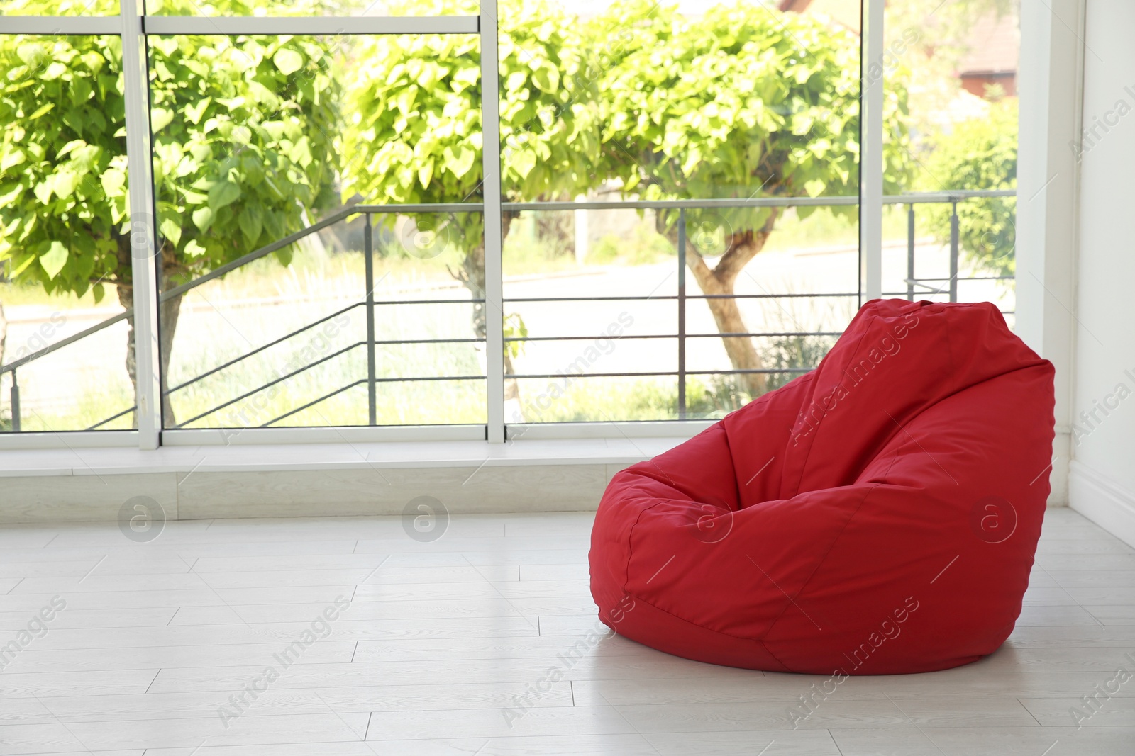 Photo of Red bean bag chair near window in room. Space for text