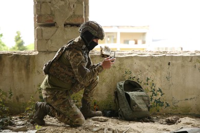 Military mission. Soldier in uniform with drone controller inside abandoned building, space for text