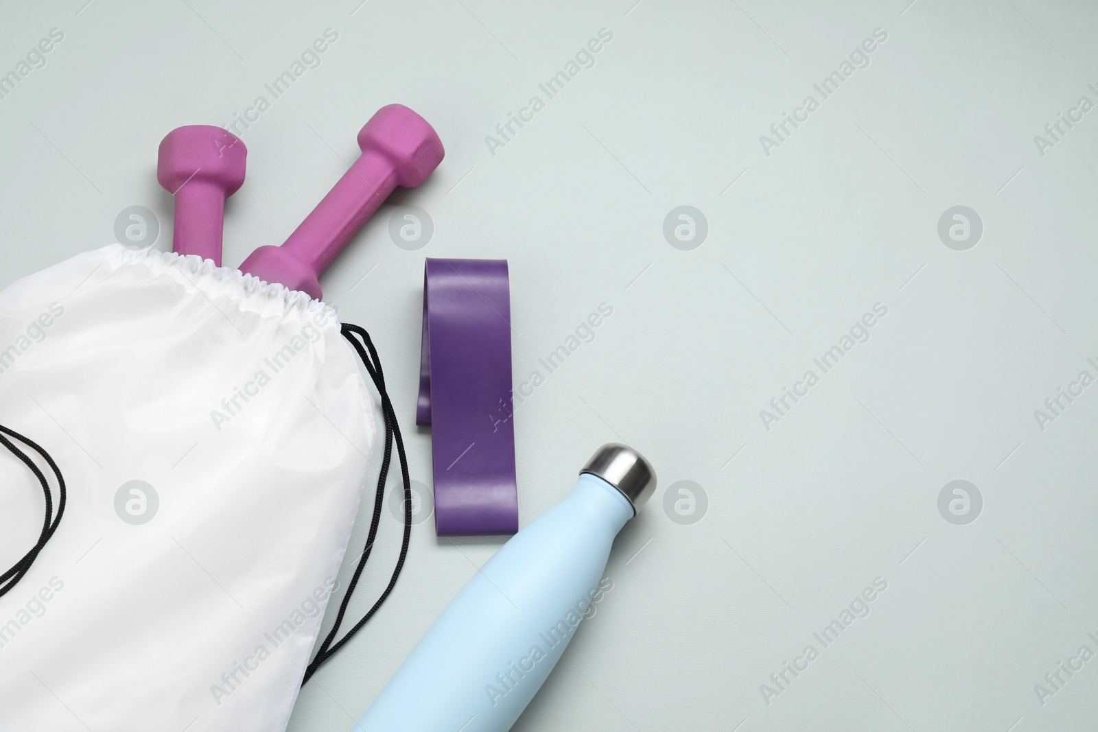 Photo of White drawstring bag, thermo bottle, fitness elastic band and dumbbells on light background, above view. Space for text