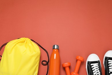 Photo of Yellow drawstring bag, thermo bottle, sneakers and dumbbells on crimson background, flat lay. Space for text