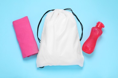 Photo of White drawstring bag, bottle and cloth on light blue background, flat lay