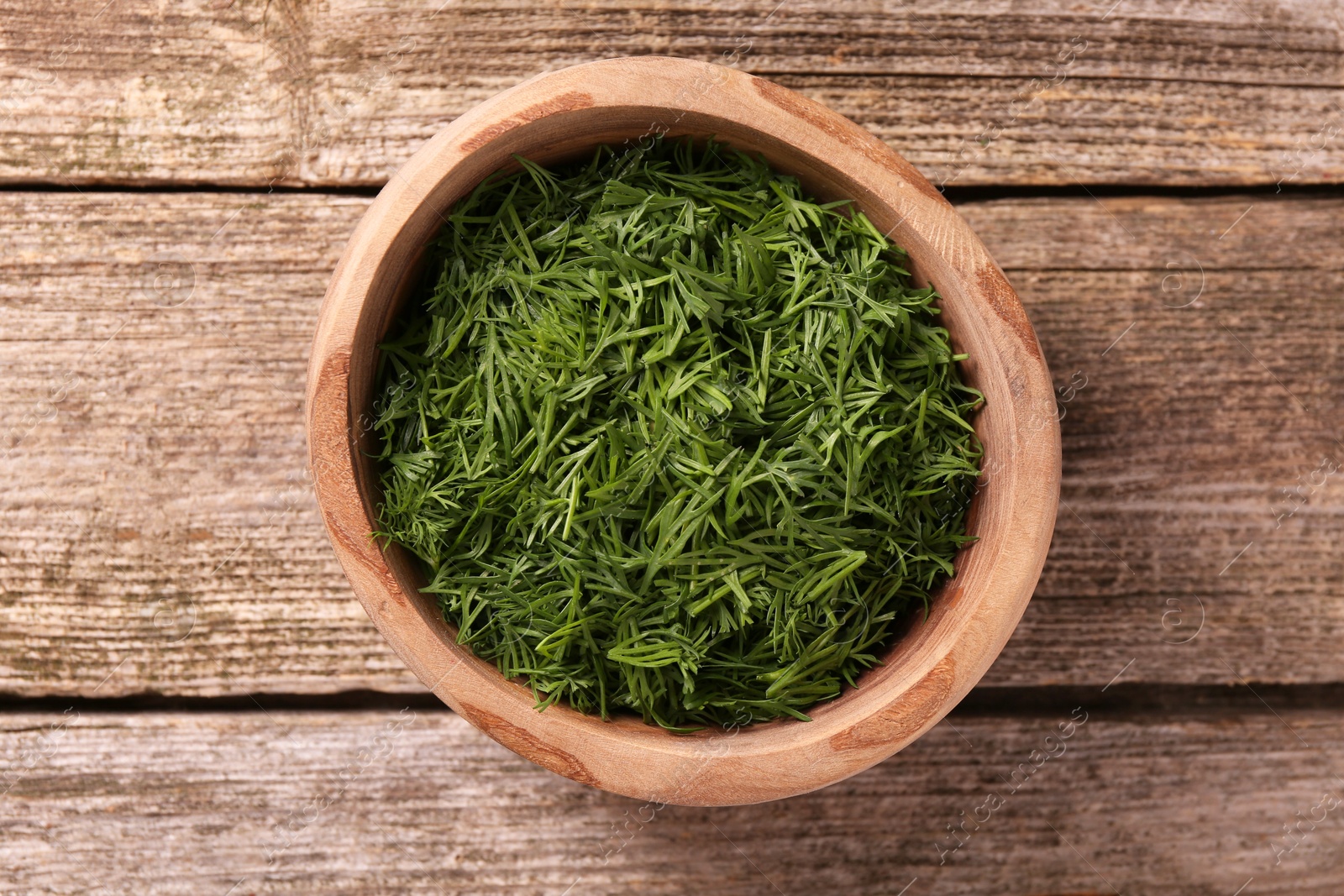 Photo of Fresh cut dill in bowl on wooden table, top view