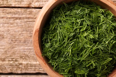 Photo of Fresh cut dill in bowl on wooden table, top view. Space for text