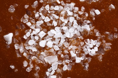 Photo of Delicious caramel sauce with sea salt as background, top view