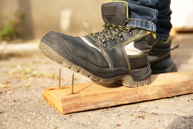 Photo of Careless worker stepping on nails in wooden plank outdoors, closeup