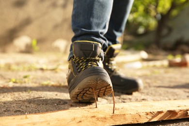 Careless worker stepping on nail in wooden plank outdoors, closeup