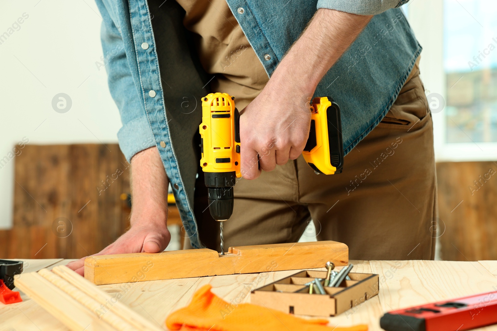 Photo of Craftsman working with drill at wooden table in workshop, closeup