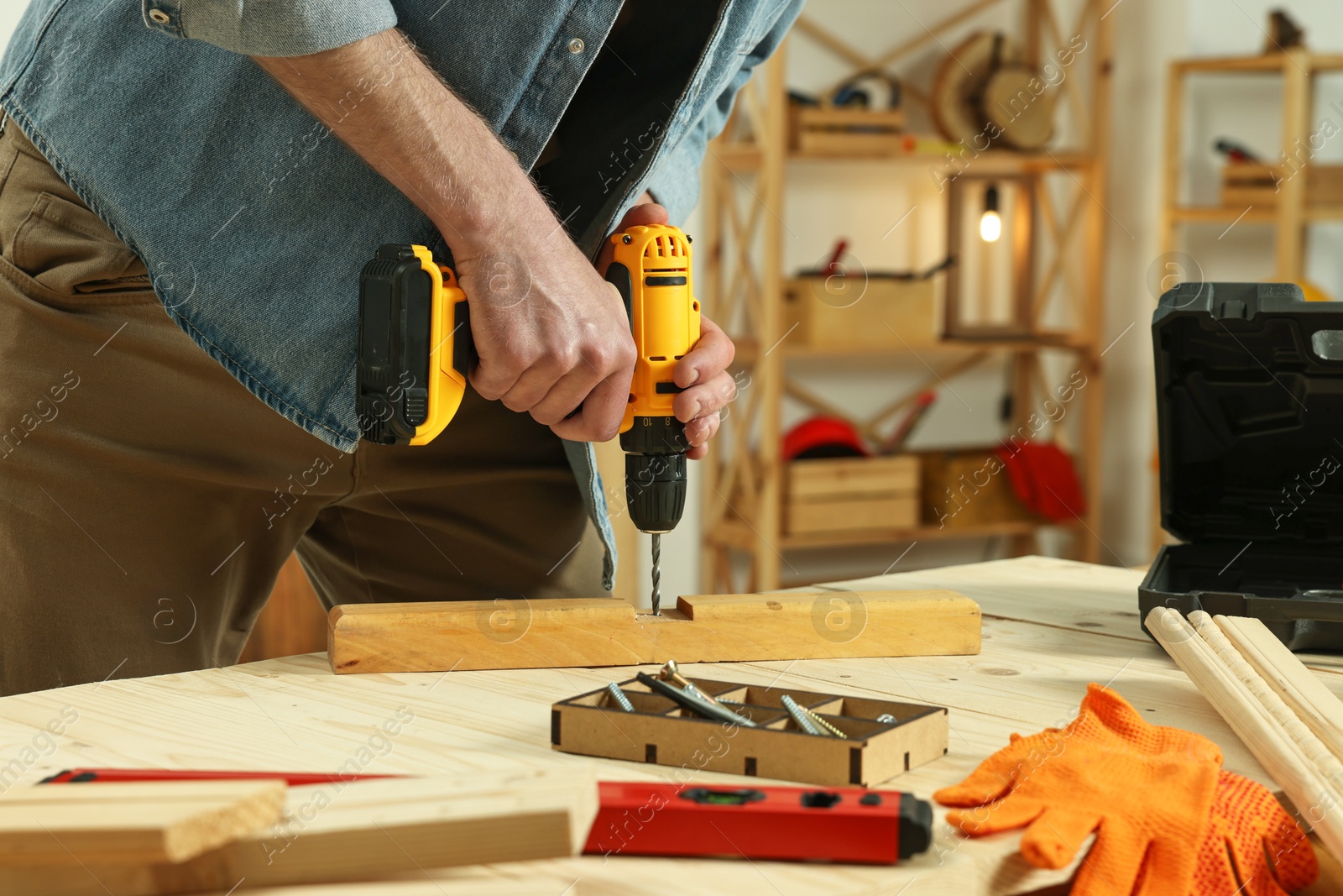 Photo of Craftsman working with drill at wooden table in workshop, closeup