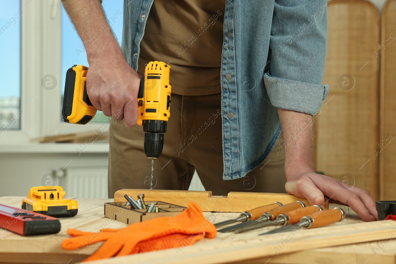 Photo of Craftsman working with drill at wooden table in workshop, closeup