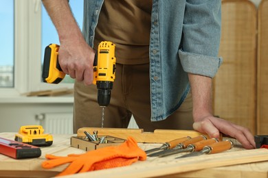 Photo of Craftsman working with drill at wooden table in workshop, closeup