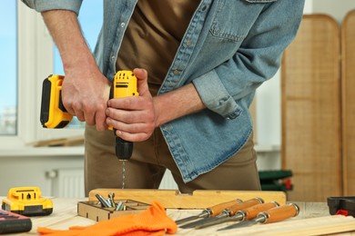 Photo of Craftsman working with drill at wooden table in workshop, closeup