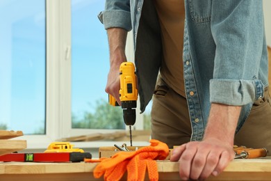 Photo of Craftsman working with drill at wooden table in workshop, closeup