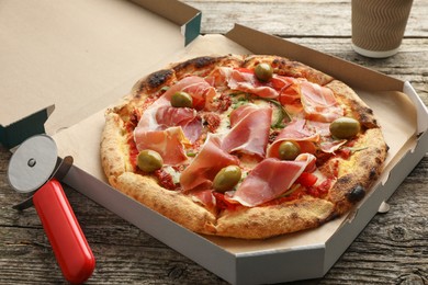 Photo of Tasty pizza with cured ham, olives, sun-dried tomato and cutter on wooden table