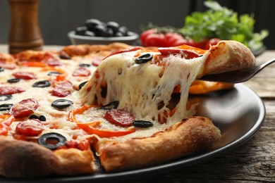 Photo of Taking piece of tasty pizza at wooden table, closeup