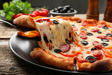 Photo of Taking piece of tasty pizza at wooden table, closeup