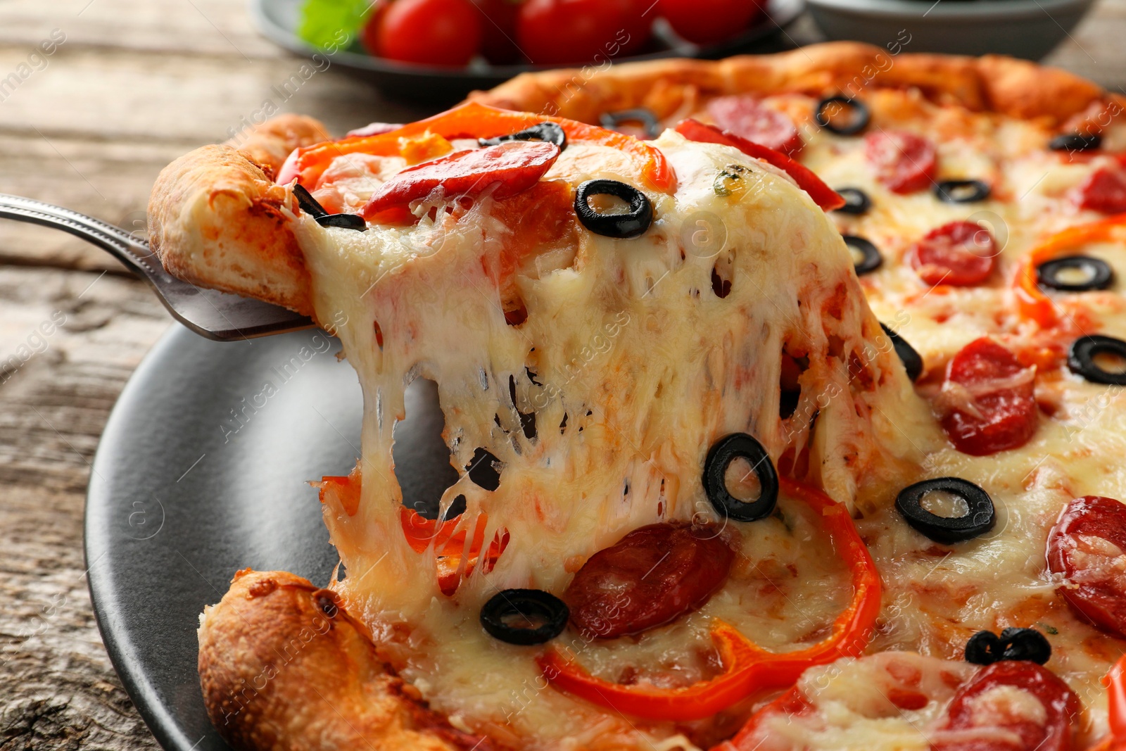 Photo of Taking piece of tasty pizza at wooden table, closeup