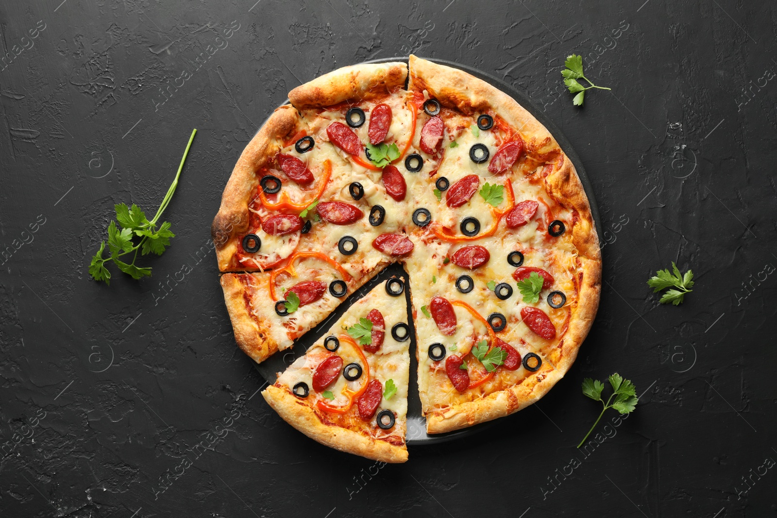 Photo of Tasty pizza with dry smoked sausages, olives, pepper and parsley on black table, top view