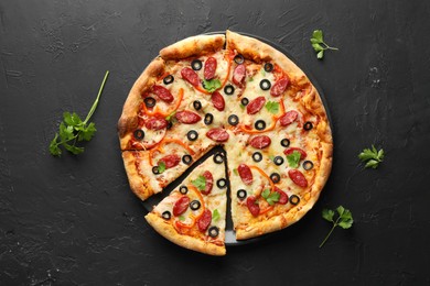 Tasty pizza with dry smoked sausages, olives, pepper and parsley on black table, top view