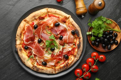 Photo of Tasty pizza with cured ham, olives, tomatoes and parsley on black table, top view