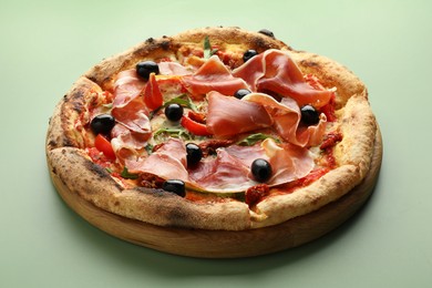 Photo of Tasty pizza with cured ham, olives and sun-dried tomato on green background