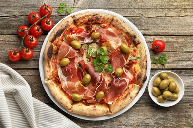 Photo of Tasty pizza with cured ham, olives, tomatoes and parsley on wooden table, top view