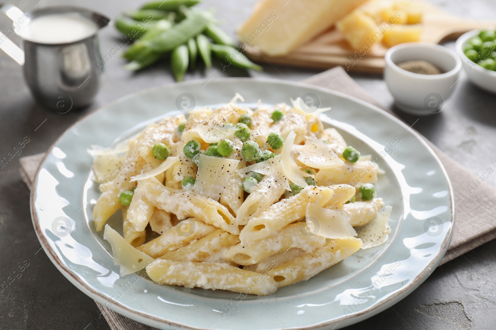 Photo of Delicious pasta with green peas, cheese, creamy sauce and ground pepper on grey table