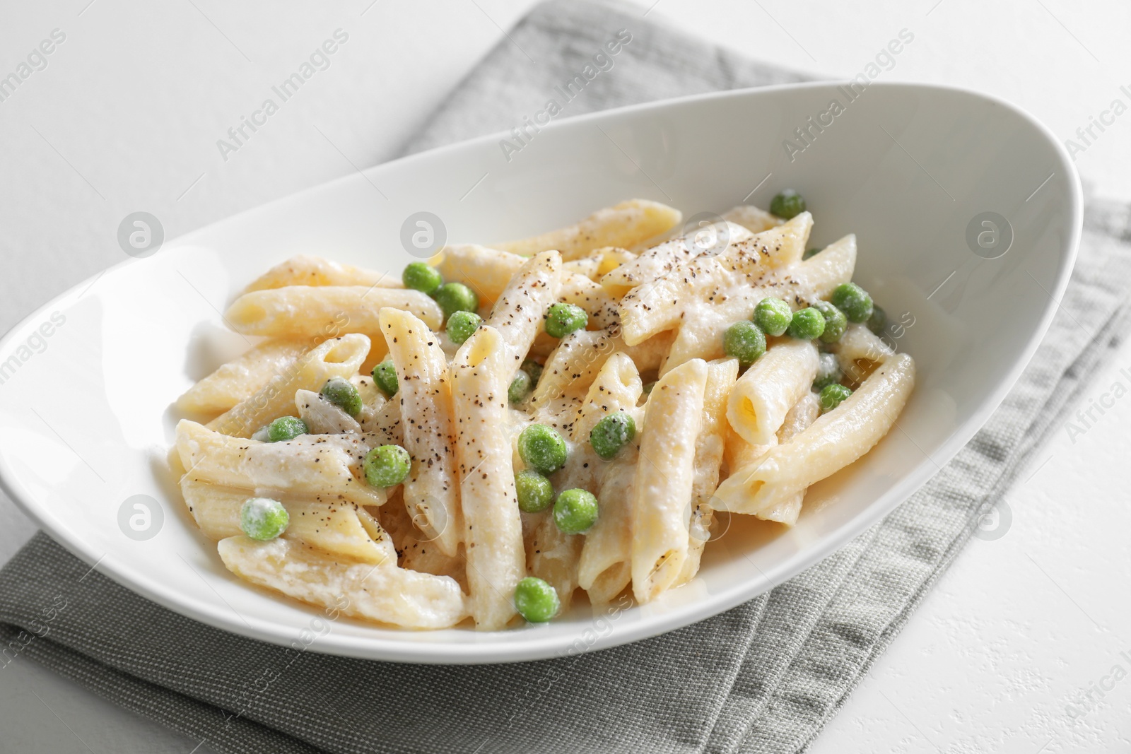 Photo of Delicious pasta with green peas and creamy sauce in bowl on white table