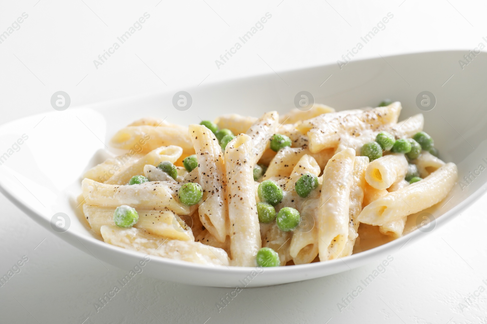 Photo of Delicious pasta with green peas and creamy sauce in bowl on white table