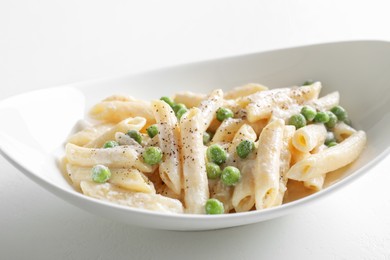 Photo of Delicious pasta with green peas and creamy sauce in bowl on white table