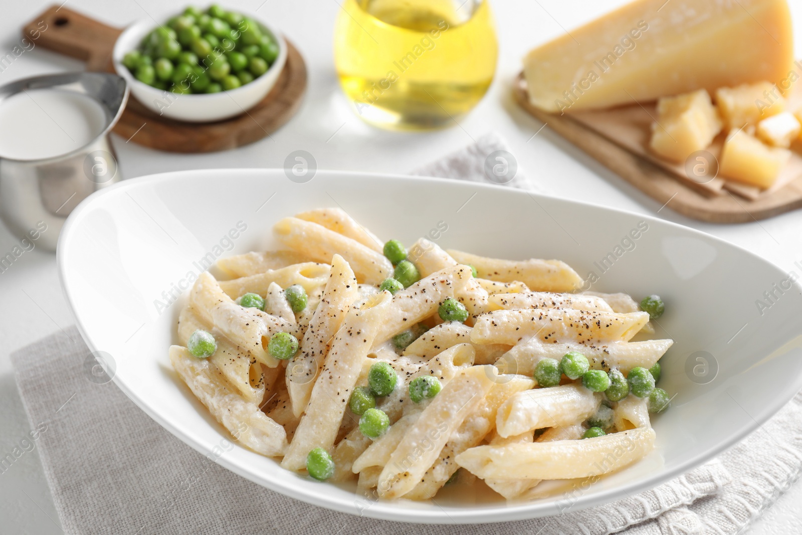 Photo of Delicious pasta with green peas and creamy sauce in bowl on white table