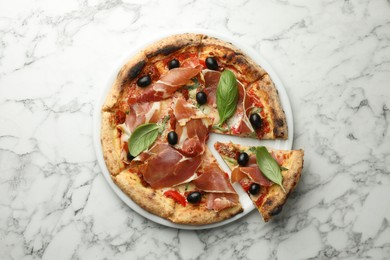 Tasty pizza with cured ham, olives, sun-dried tomato and basil on white marble table, top view