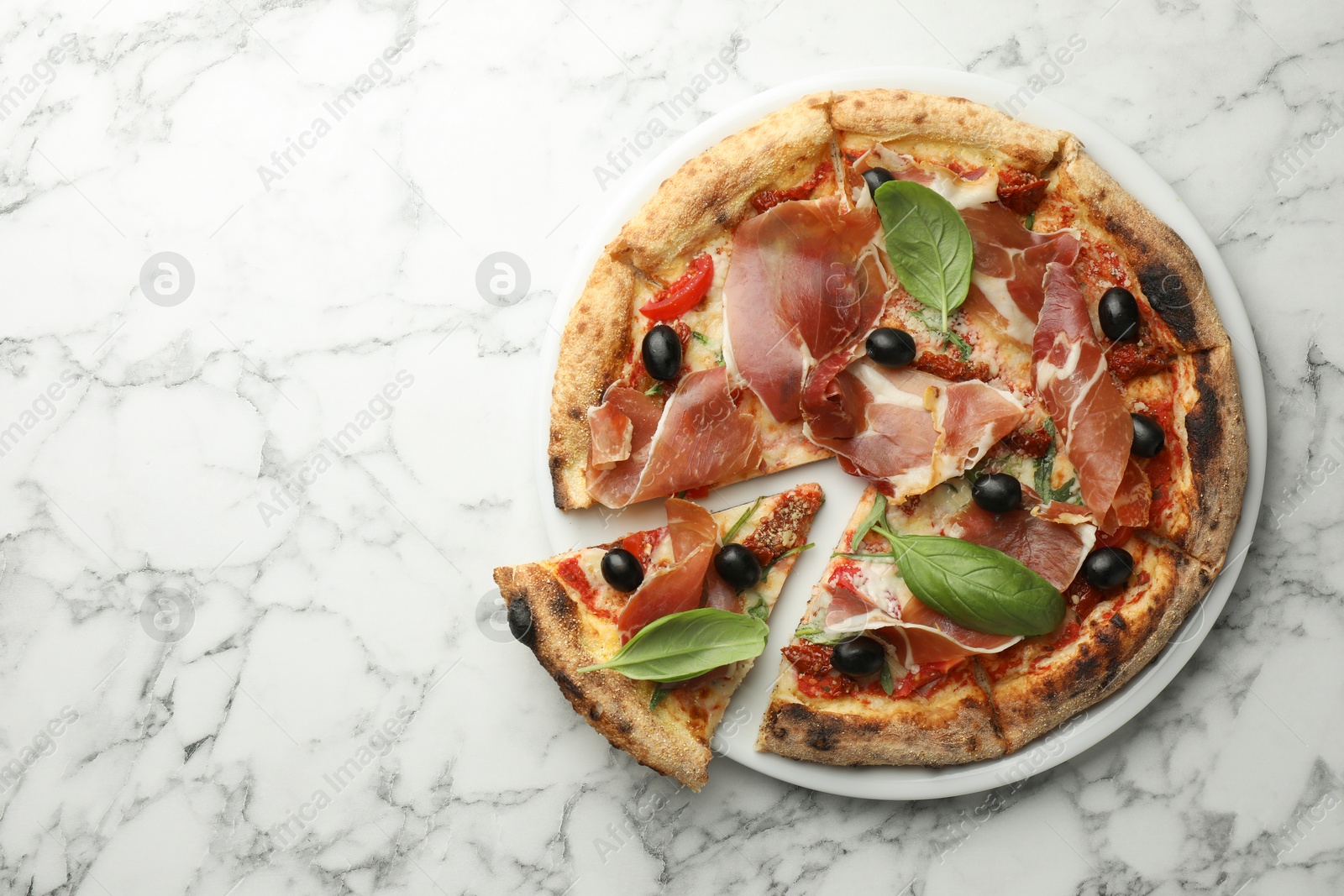 Photo of Tasty pizza with cured ham, olives, sun-dried tomato and basil on white marble table, top view. Space for text