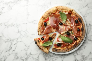 Tasty pizza with cured ham, olives, sun-dried tomato and basil on white marble table, top view. Space for text