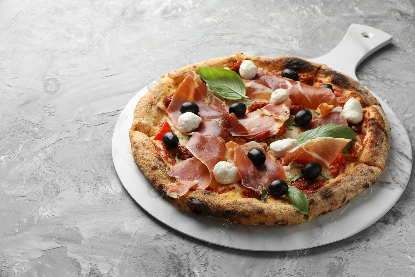 Photo of Tasty pizza with cured ham, olives, mozzarella cheese, sun-dried tomato and basil on gray textured table