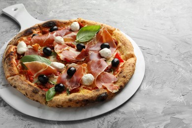 Photo of Tasty pizza with cured ham, olives, mozzarella cheese, sun-dried tomato and basil on gray textured table