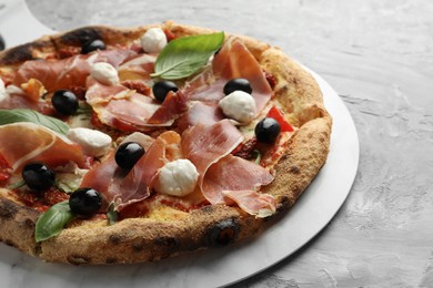 Tasty pizza with cured ham, olives, mozzarella cheese, sun-dried tomato and basil on gray textured table, closeup