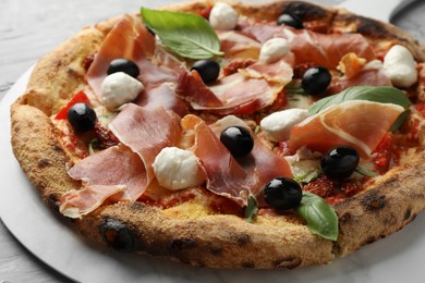 Photo of Tasty pizza with cured ham, olives, mozzarella cheese, sun-dried tomato and basil on table, closeup