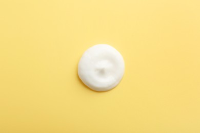 Photo of Drop of face cream on yellow background, top view