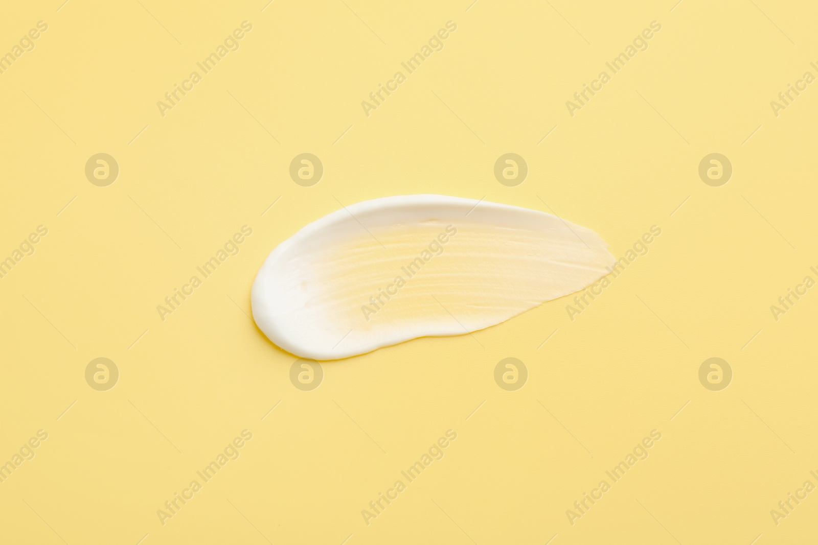 Photo of Sample of face cream on yellow background, top view