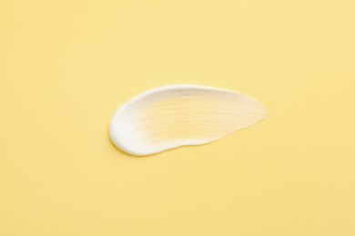 Photo of Sample of face cream on yellow background, top view