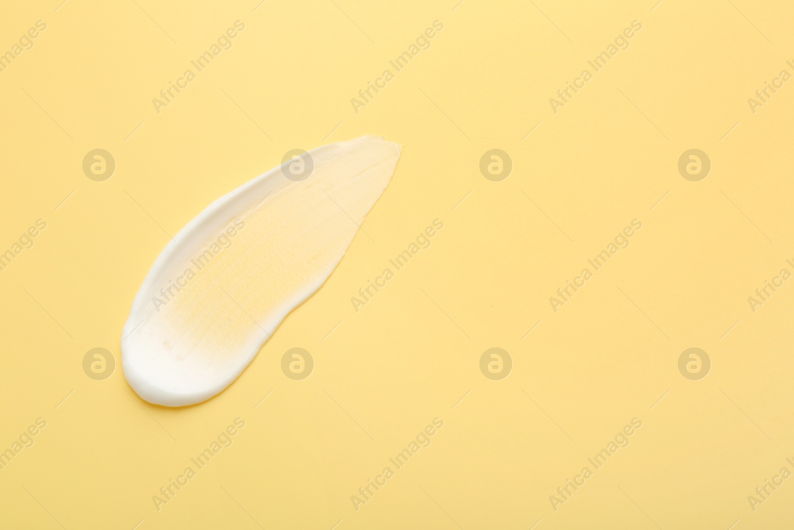 Photo of Sample of face cream on yellow background, top view. Space for text