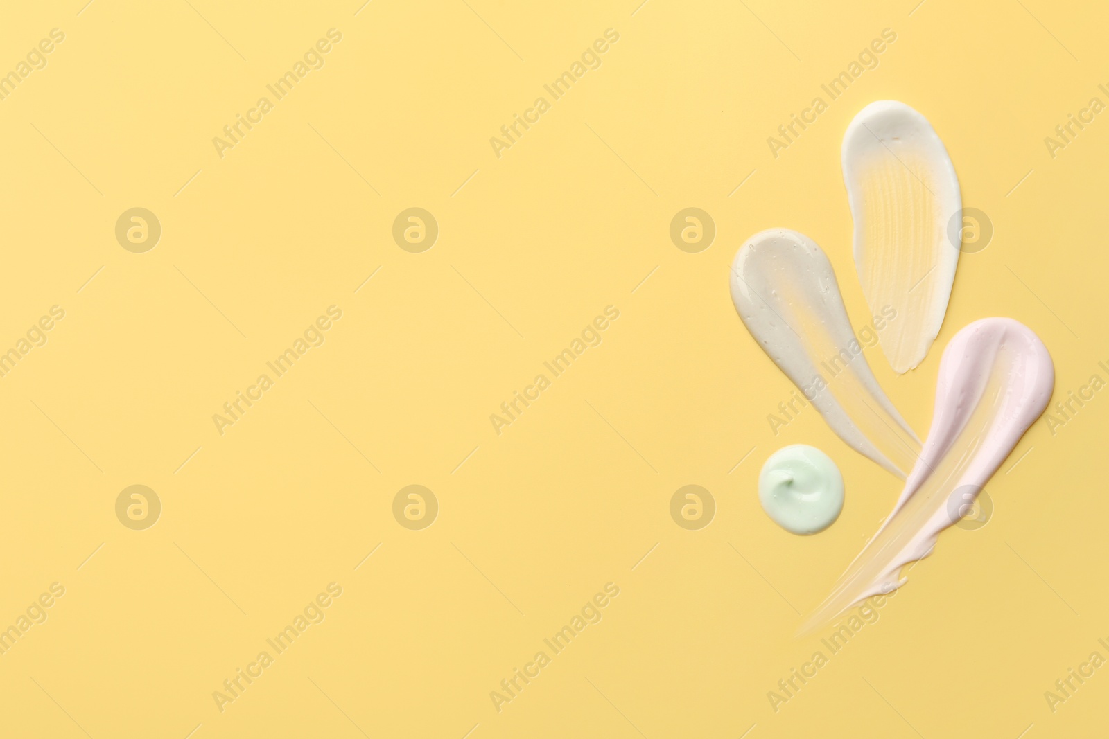 Photo of Samples of face cream on yellow background, top view. Space for text