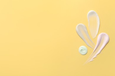 Photo of Samples of face cream on yellow background, top view. Space for text