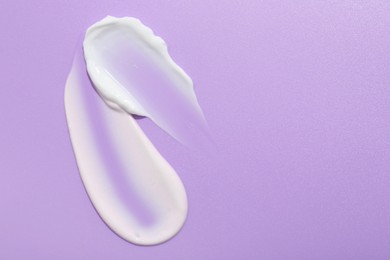 Photo of Samples of face cream on violet background, top view. Space for text