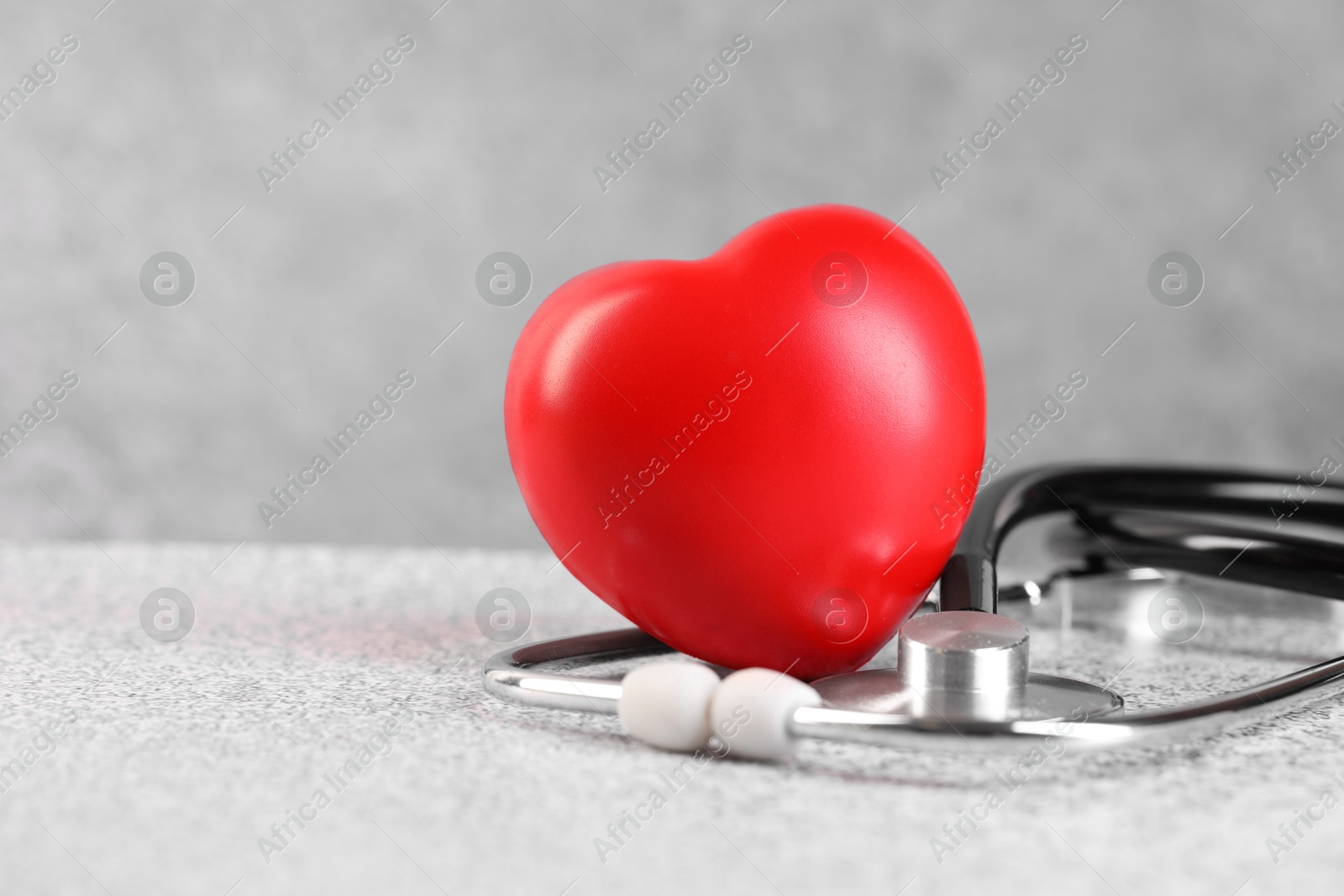 Photo of Stethoscope and red heart on grey stone table. Space for text