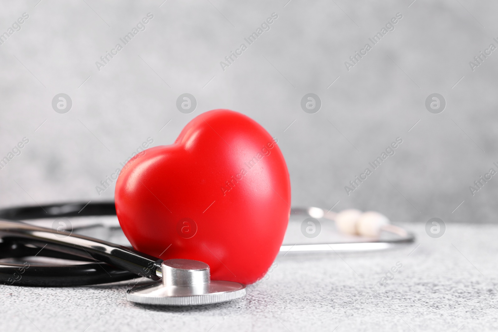 Photo of Stethoscope and red heart on grey stone table, closeup. Space for text