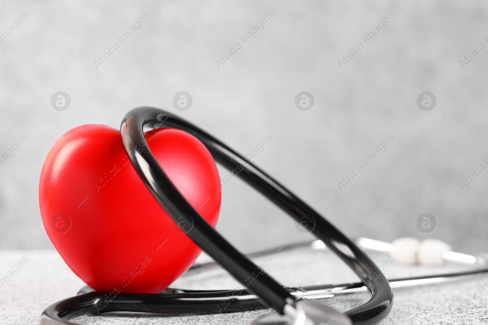 Photo of Stethoscope and red heart on grey stone table, closeup. Space for text